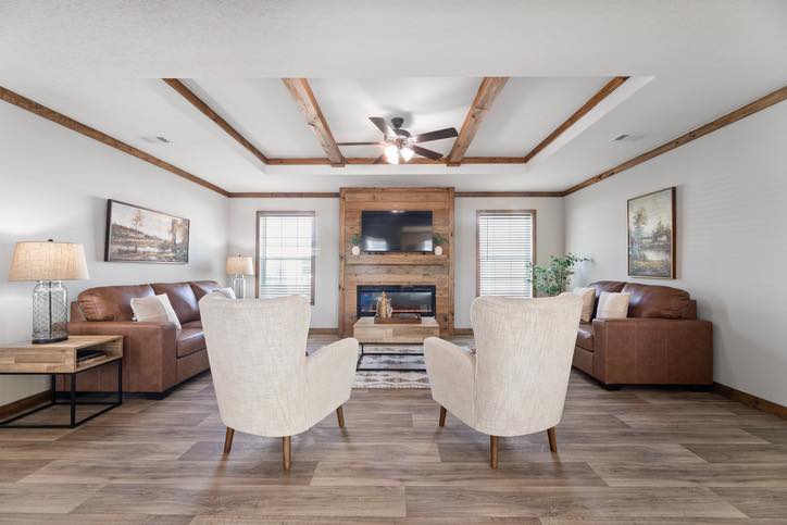 Spacious living room with wooden floors features two white armchairs facing a wooden fireplace. Two brown sofas flank the room, creating a cozy atmosphere.