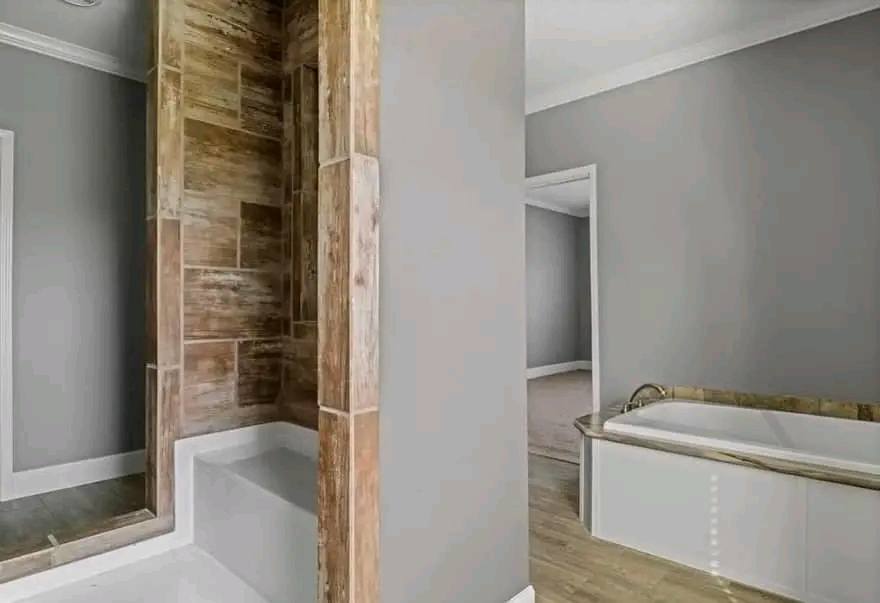 A modern bathroom with gray walls features a wood-tiled shower and a white bathtub with a wood accent. The space is open, bright, and minimalistic.