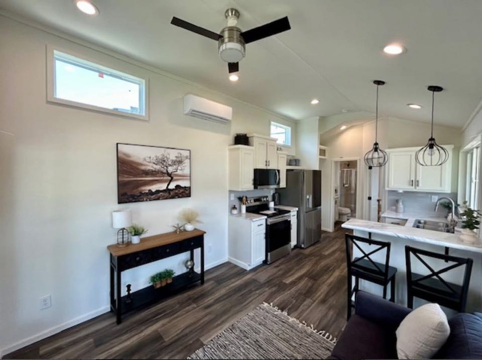 Modern kitchen and living area with white cabinets, stainless steel appliances, and a ceiling fan. Hardwood floors and pendant lights create a cozy ambiance.