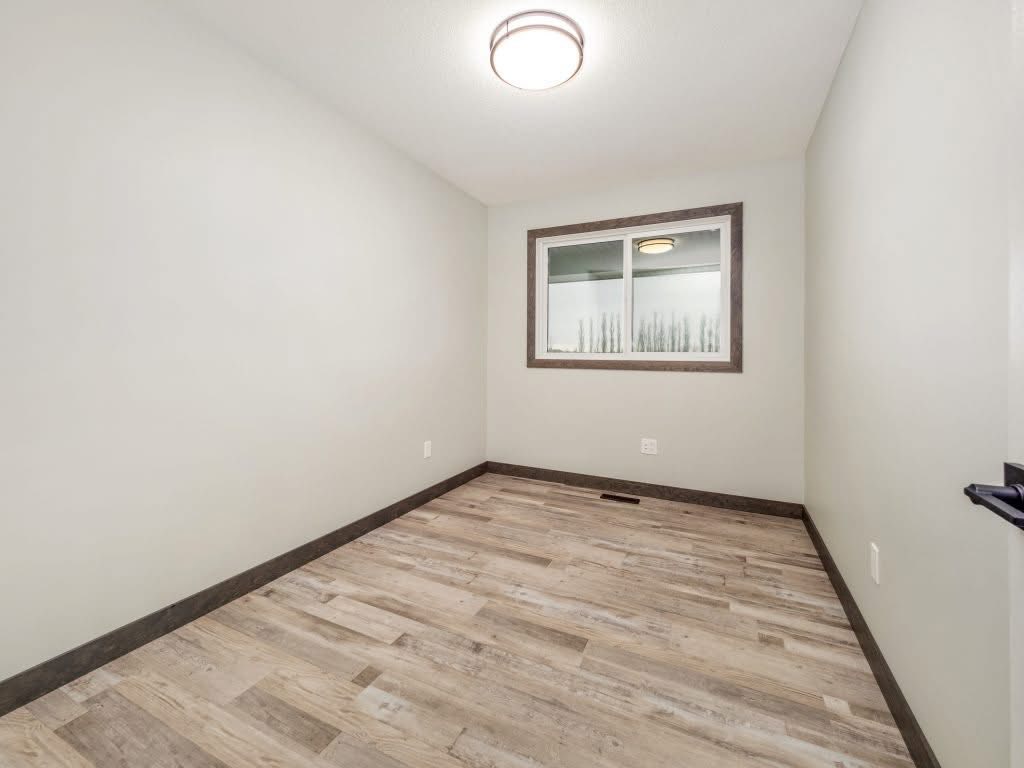 Minimalist room with light wooden floors, gray walls, and a central ceiling light. A window with a wooden frame offers a glimpse outside. Peaceful vibe.