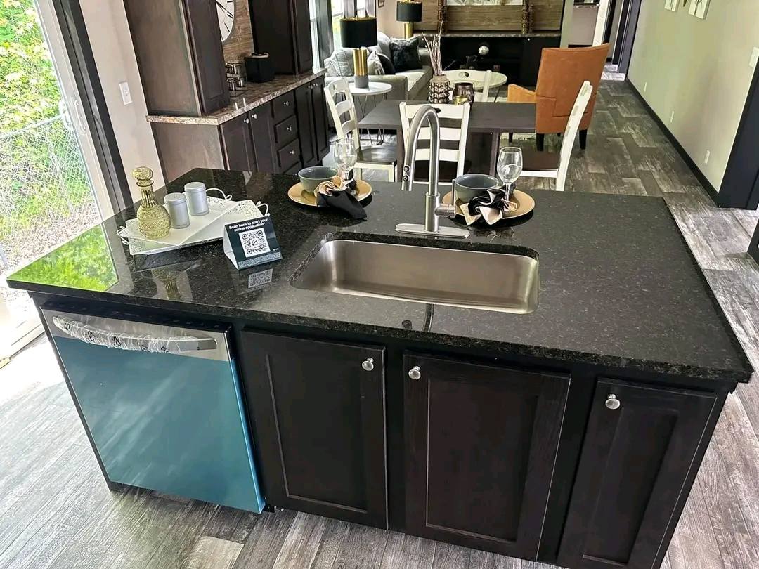 Modern kitchen with a dark granite island countertop, a stainless steel sink, and a dishwasher. A dining area with elegant table settings is visible.