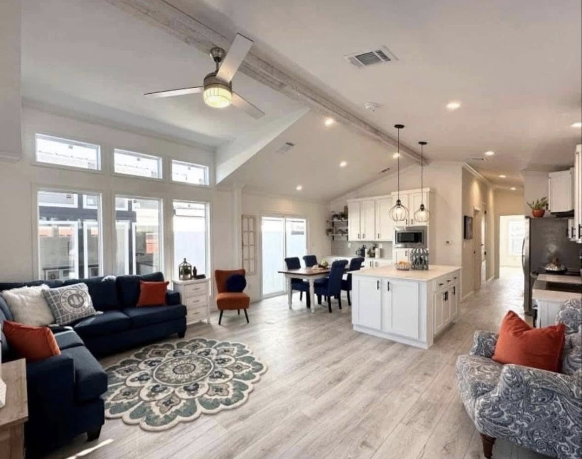 Bright, open-plan living area with a navy sofa and orange accents on the left. A kitchen with white cabinetry and pendant lights is on the right.