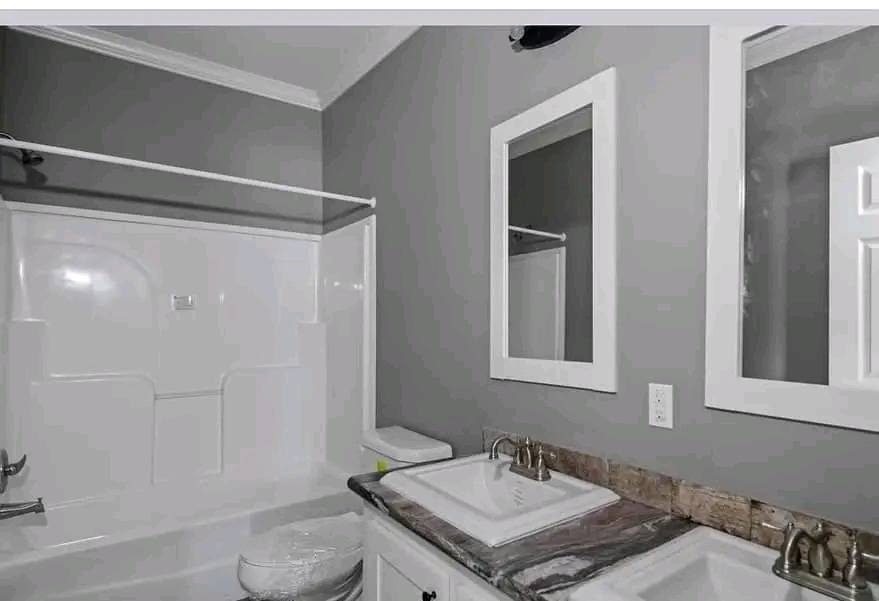 Modern bathroom with gray walls features a white bathtub, dual sinks with marble countertops, and two mirrors above. Bright, clean, and organized space.