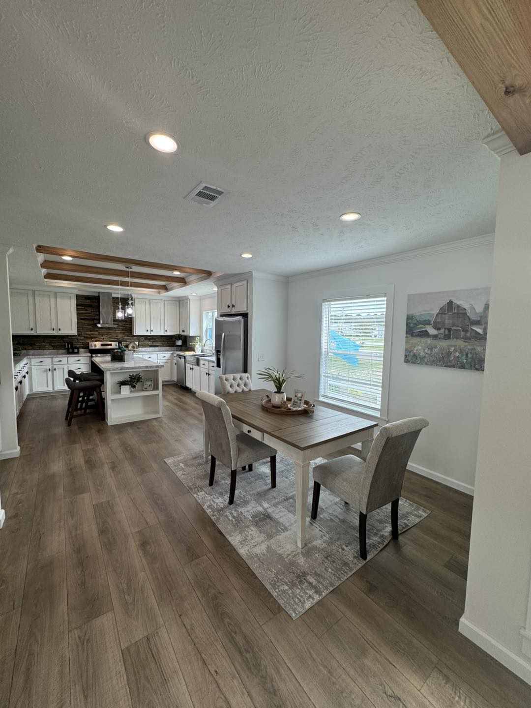 Spacious kitchen and dining area with wooden floors. Elegant table with two chairs on a rug, white cabinets, and modern appliances under soft lighting. Cozy ambiance.