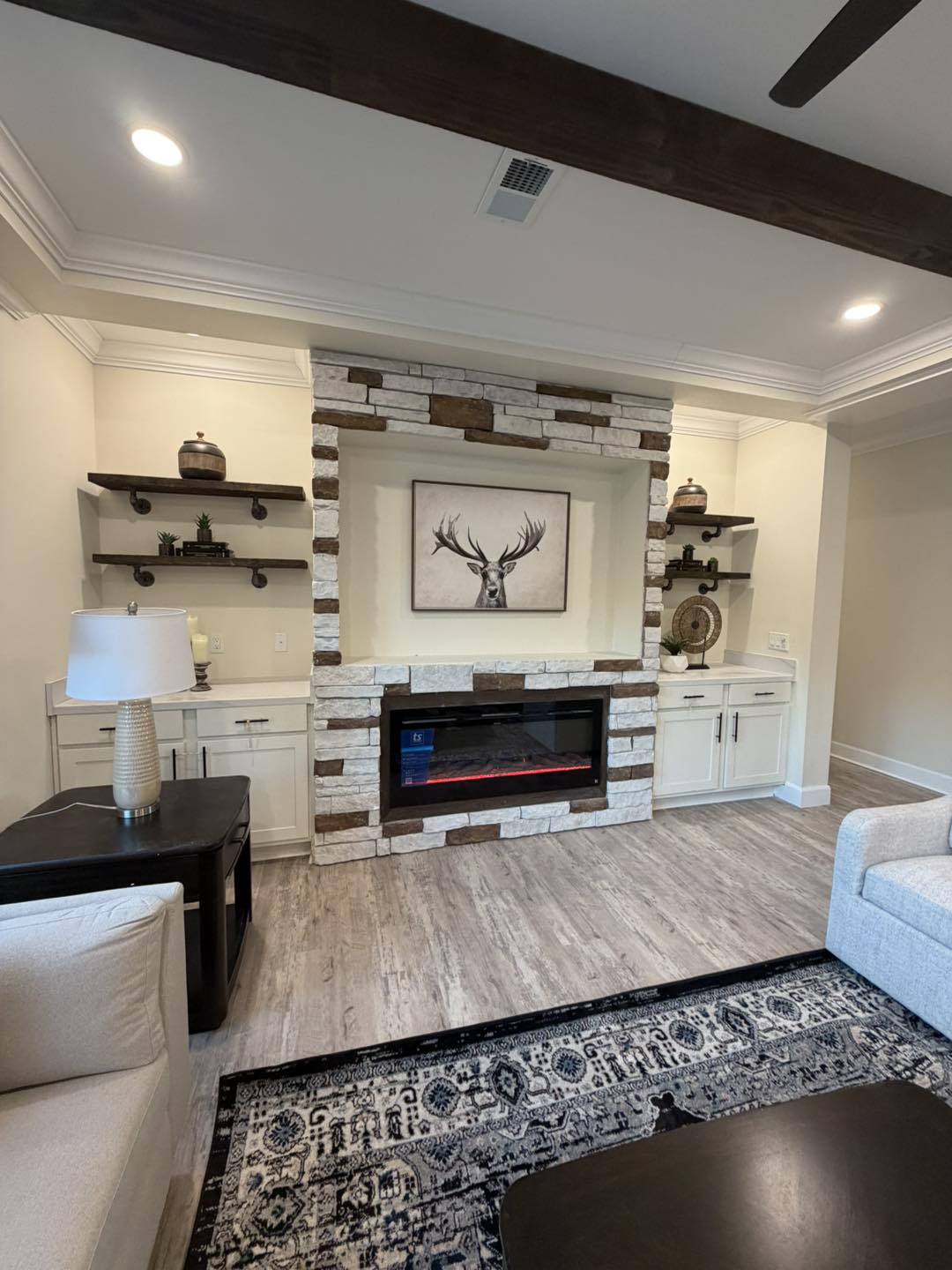 Cozy living room featuring a stone fireplace with a deer artwork above. Surrounding shelves hold decorative items, exuding a warm, inviting atmosphere.