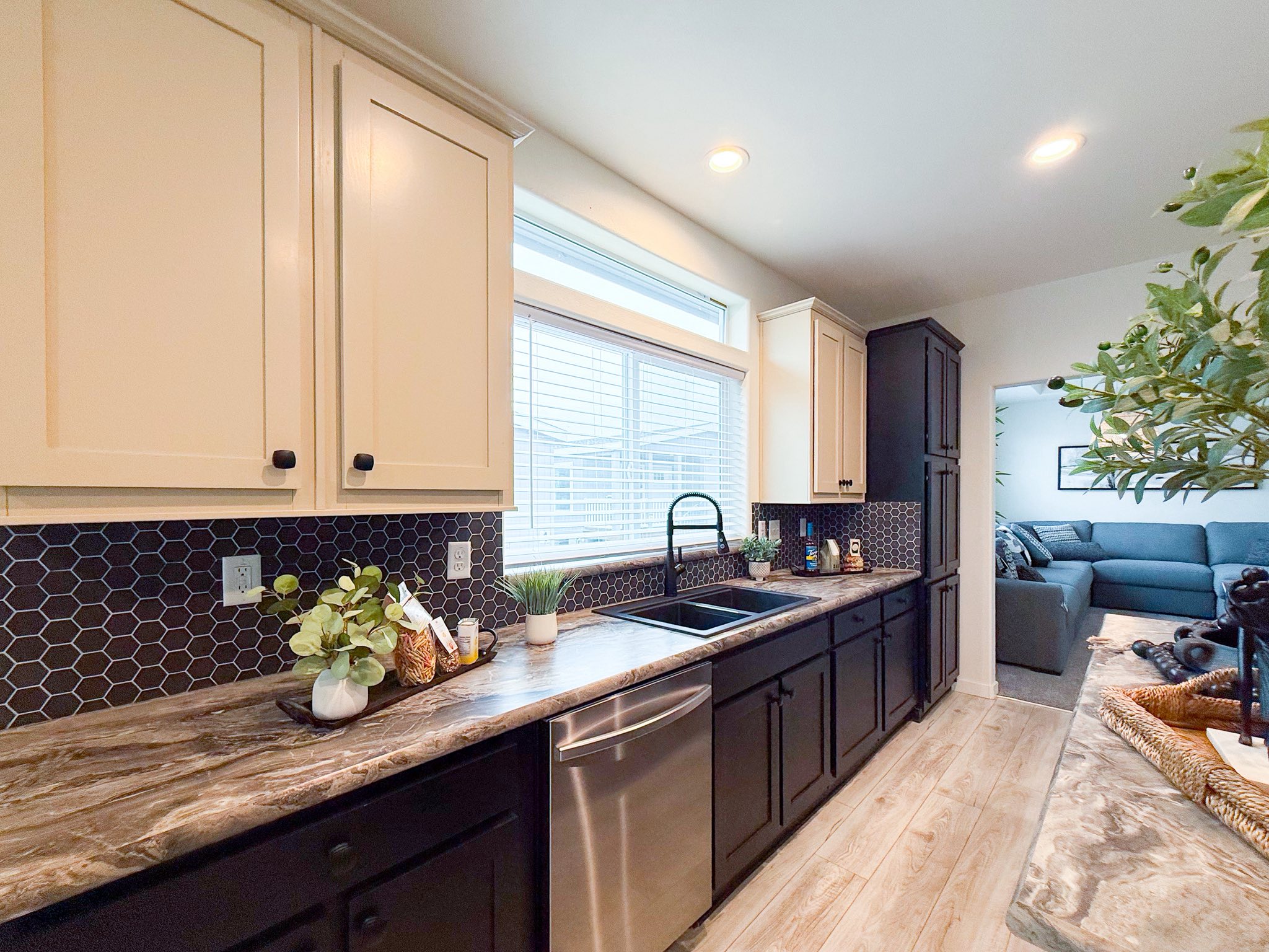 Bright kitchen with white upper cabinets, black lower cabinets, and a marble countertop. A large window, plants, and decor create a cozy ambiance.