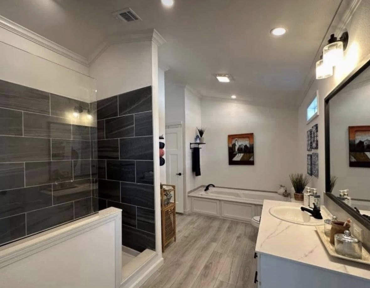 Modern bathroom with gray tile shower, marble-topped vanity, and a bathtub. Neutral tones, abstract art, and plants add elegance and calm.