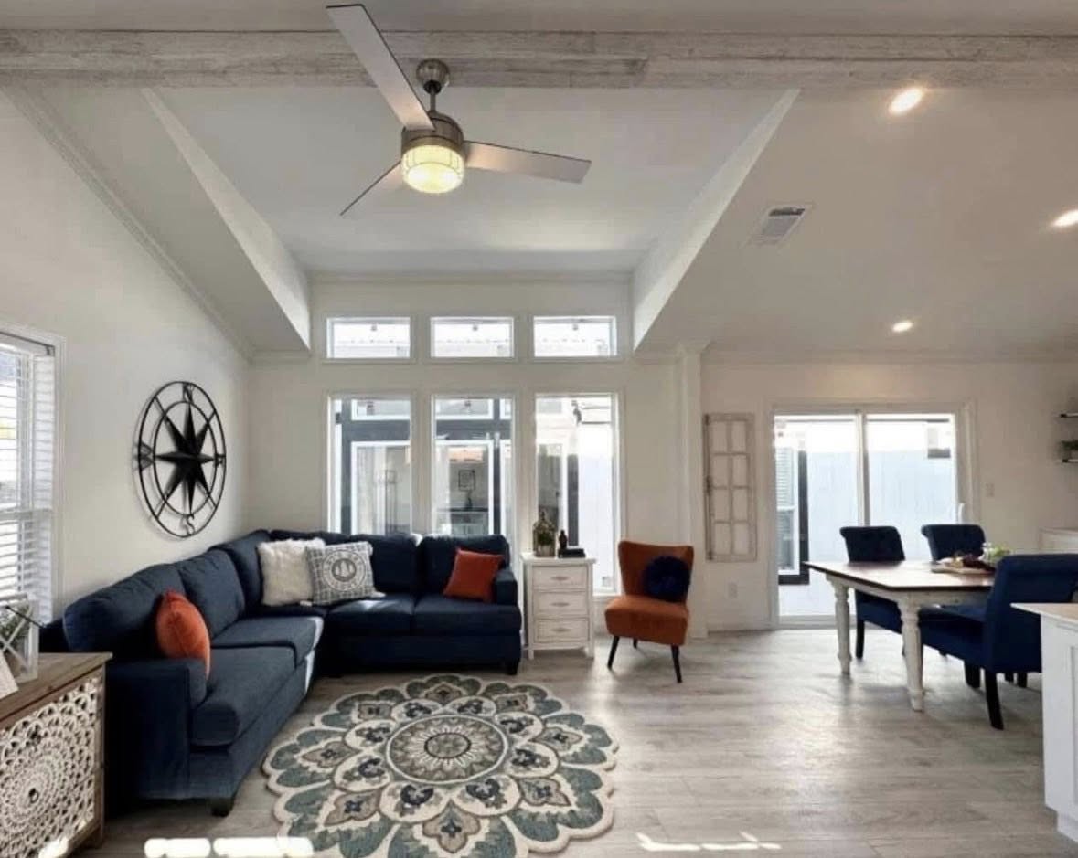 Spacious living room with vaulted ceilings, a navy sectional, and vibrant orange and blue accents. A geometric rug centers the room, exuding a cozy, modern vibe.