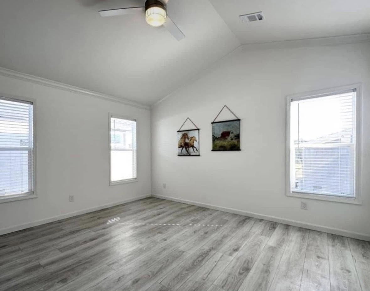 Spacious, bright room with light gray wood flooring and a vaulted ceiling. Two windows and two horse-themed paintings create a serene atmosphere.