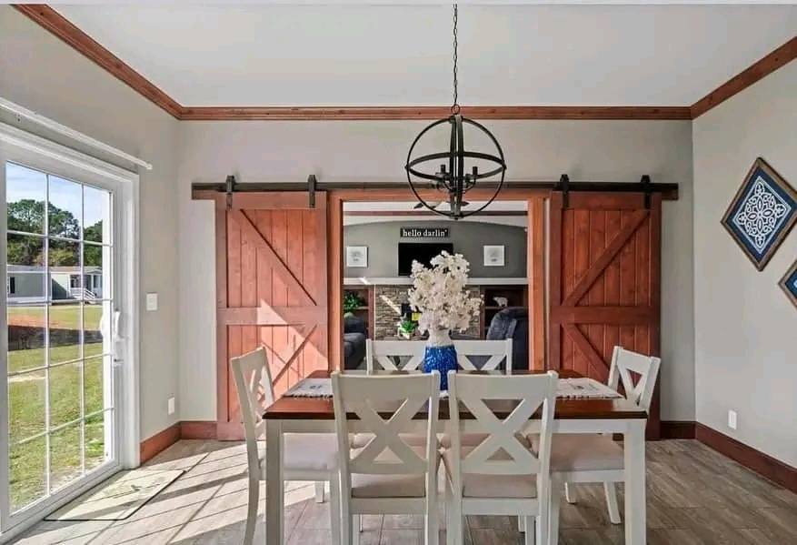 Bright dining room with white table and chairs, a blue vase with flowers, sliding barn doors, and a modern chandelier, creating a cozy ambiance.