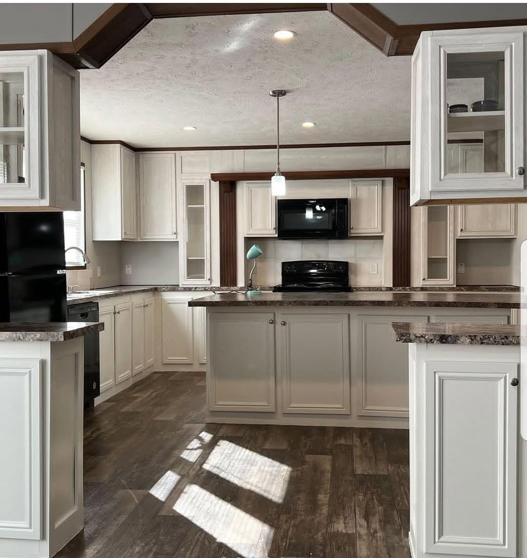 Spacious kitchen with white cabinets, dark wood floors, and a marble countertop. A black stove and microwave are centered, with modern pendant lighting.