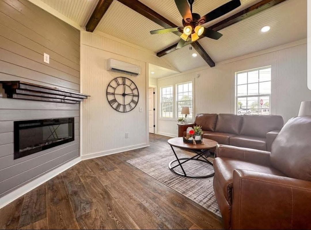 Cozy living room with brown leather sofas, round wooden coffee table, and a large wall clock. A fireplace adds warmth to the neutral decor.