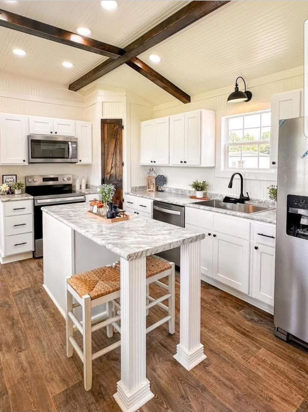 Bright, modern farmhouse kitchen with white cabinets, marble counters, and wood accents. Central island has seating. Inviting, warm, and well-lit atmosphere.