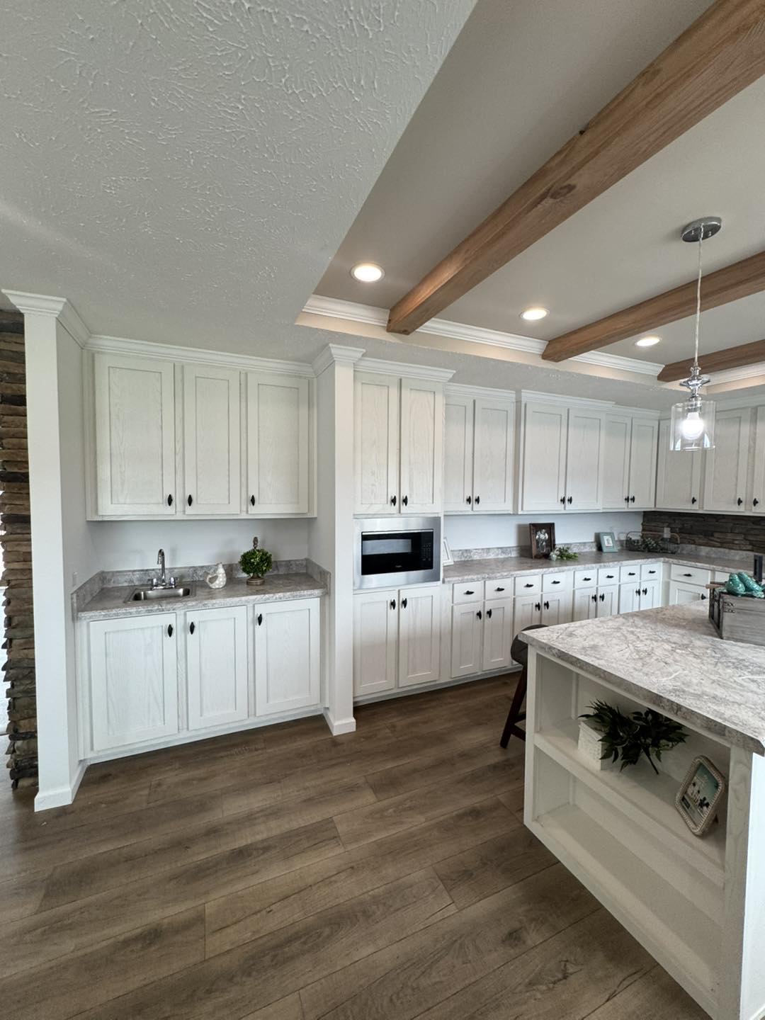 Bright kitchen with white cabinets and marble countertops. Wooden beams and floor add warmth. Modern fixtures create a cozy and inviting atmosphere.