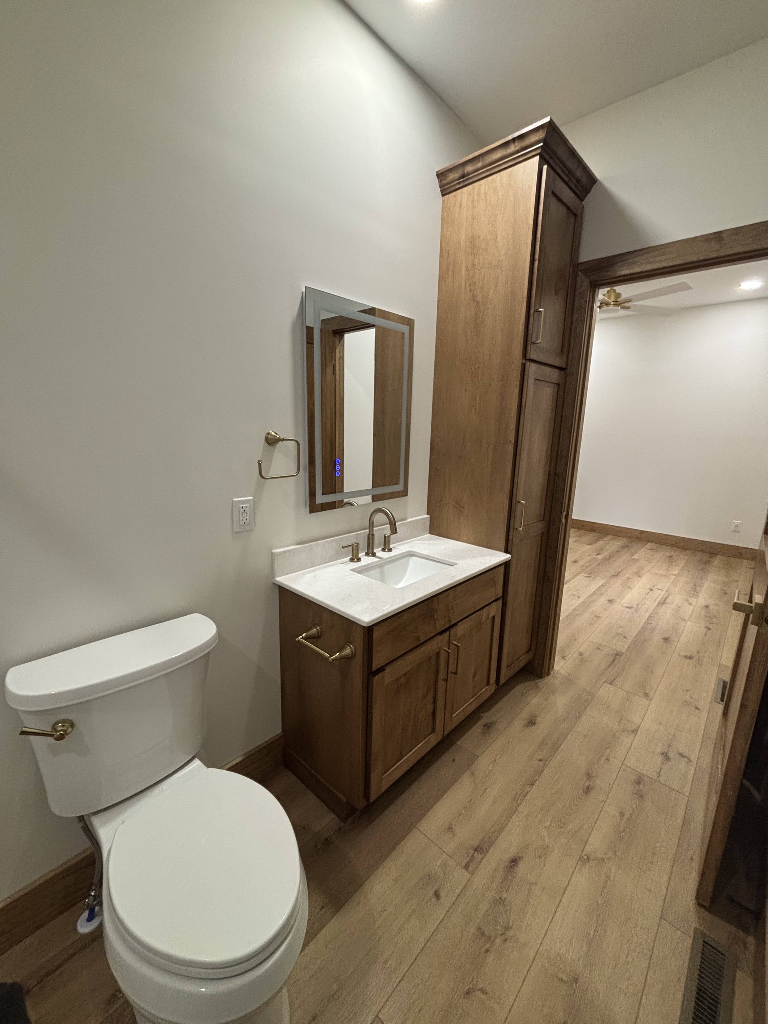 Modern bathroom with wooden floor, featuring a white toilet and a wooden vanity with a sink and mirror. The space has a minimalist and clean design.