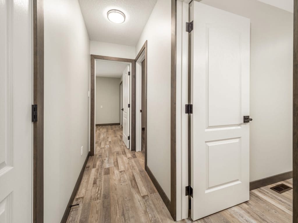 A bright hallway with light wooden floors and beige walls leads to several open white doors, creating a clean and inviting atmosphere.