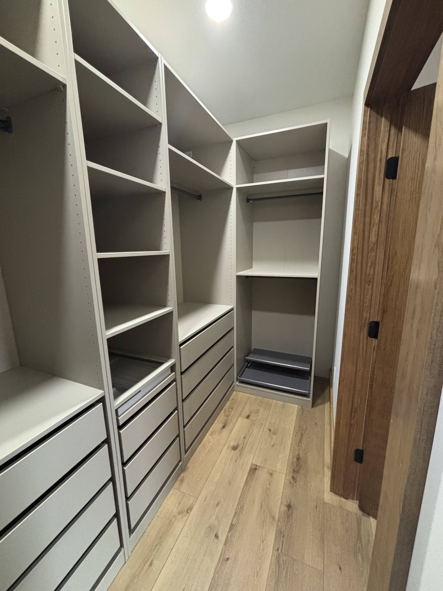 Spacious walk-in closet with light wood flooring, white wooden shelves, and drawers. Open layout conveys a clean, organized atmosphere.