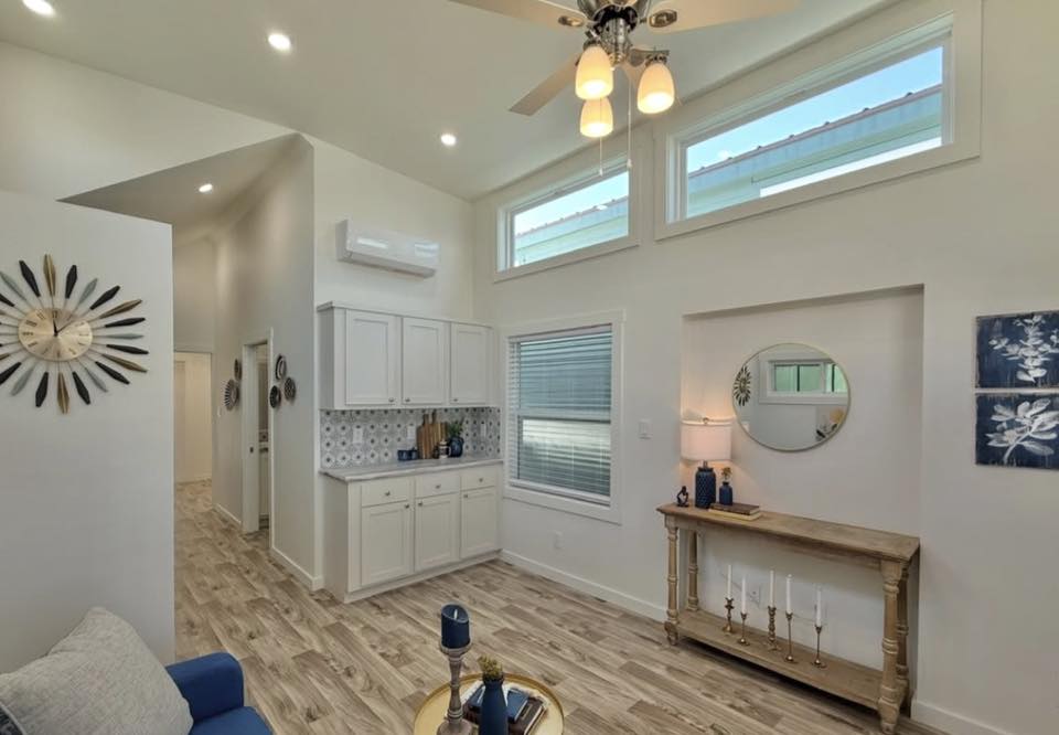 Bright, modern living room with high ceilings and natural light. Features include white cabinets, wooden flooring, wall art, and decor in blue tones. Calm ambiance.