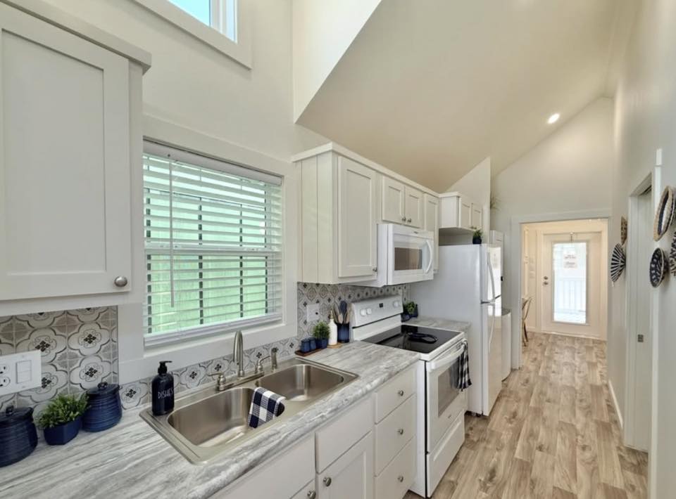 Modern, narrow kitchen with white cabinets, marble countertops, and wooden floor. A window above the sink brightens the space, creating a cozy atmosphere.