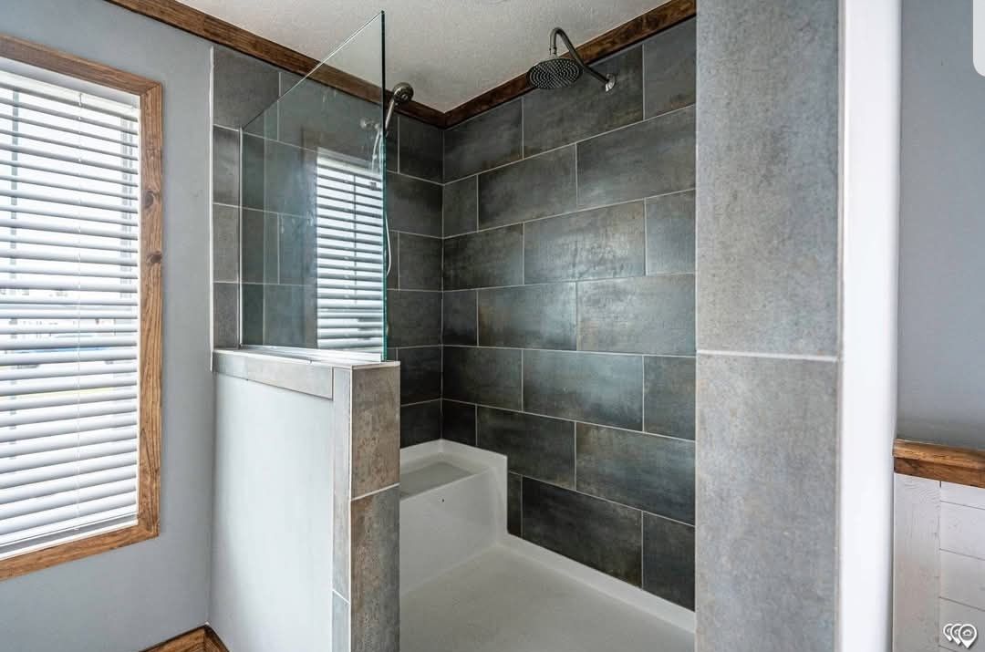 Modern shower with dark gray tiles and a glass partition. Features a rain showerhead, built-in bench, and window with blinds, creating a sleek feel.