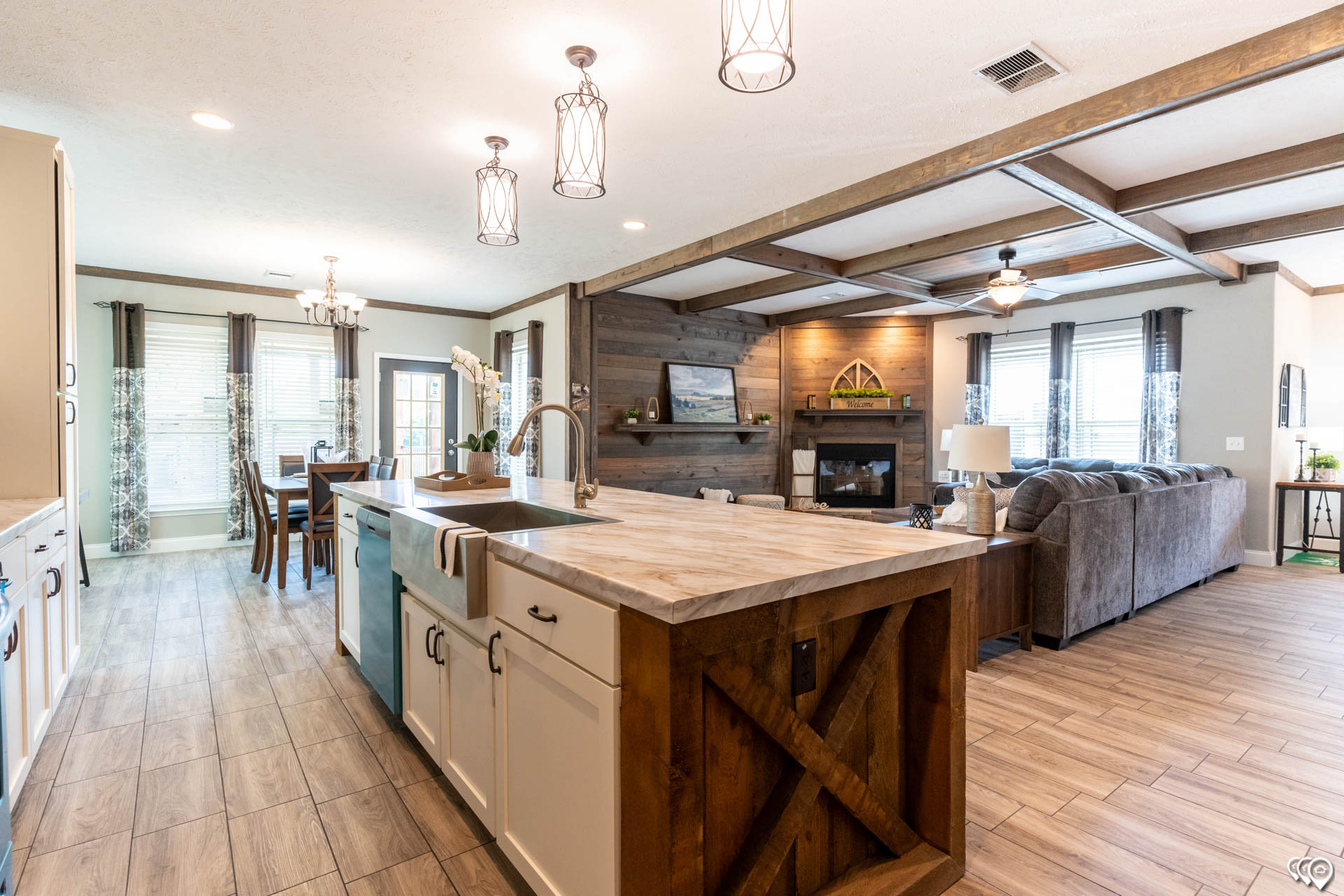 Spacious open-concept living area with a modern kitchen island, farmhouse sink, hanging lights, adjacent dining table, and cozy living room with fireplace.