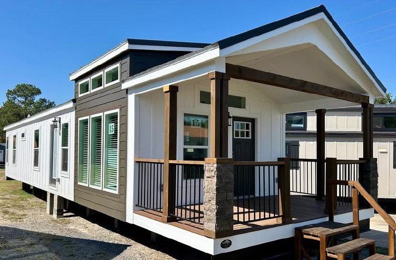 Modern tiny house with a dark and white exterior, features tall windows and a cozy front porch with wooden pillars. Sunny day and clear skies.