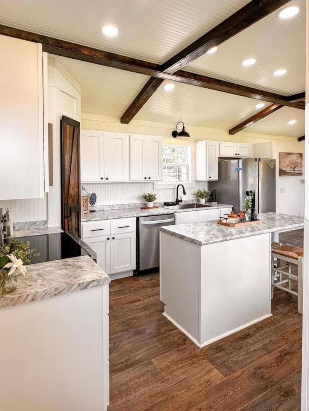 Bright kitchen with white cabinets, marble countertops, and a farmhouse sink. Exposed wooden beams on the ceiling and warm wood floors create a cozy feel.