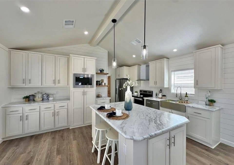 Modern kitchen with beige cabinets, marble countertops, and a central island. Pendant lights hang above. Bright, clean, and inviting atmosphere.