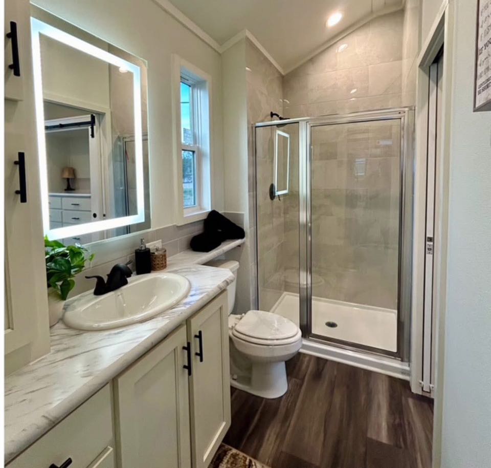 Modern bathroom with a marble countertop, round sink, and black fixtures. Glass shower, wood flooring, and plants create a fresh, inviting ambience.