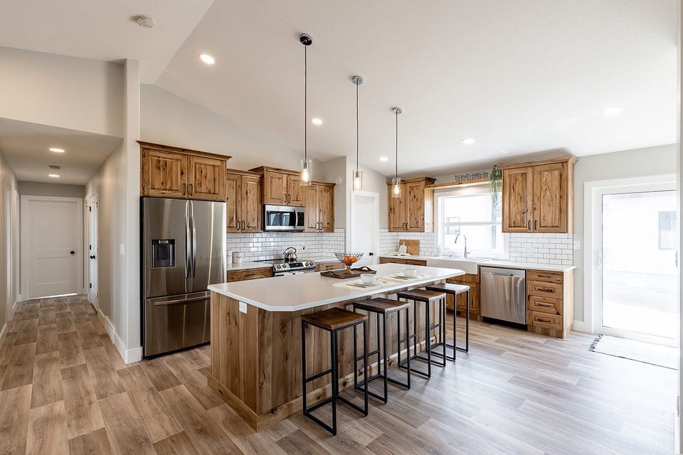 Spacious kitchen with wooden cabinets, white countertops, and stainless steel appliances. Features an island with barstools and pendant lights. Cozy, modern feel.