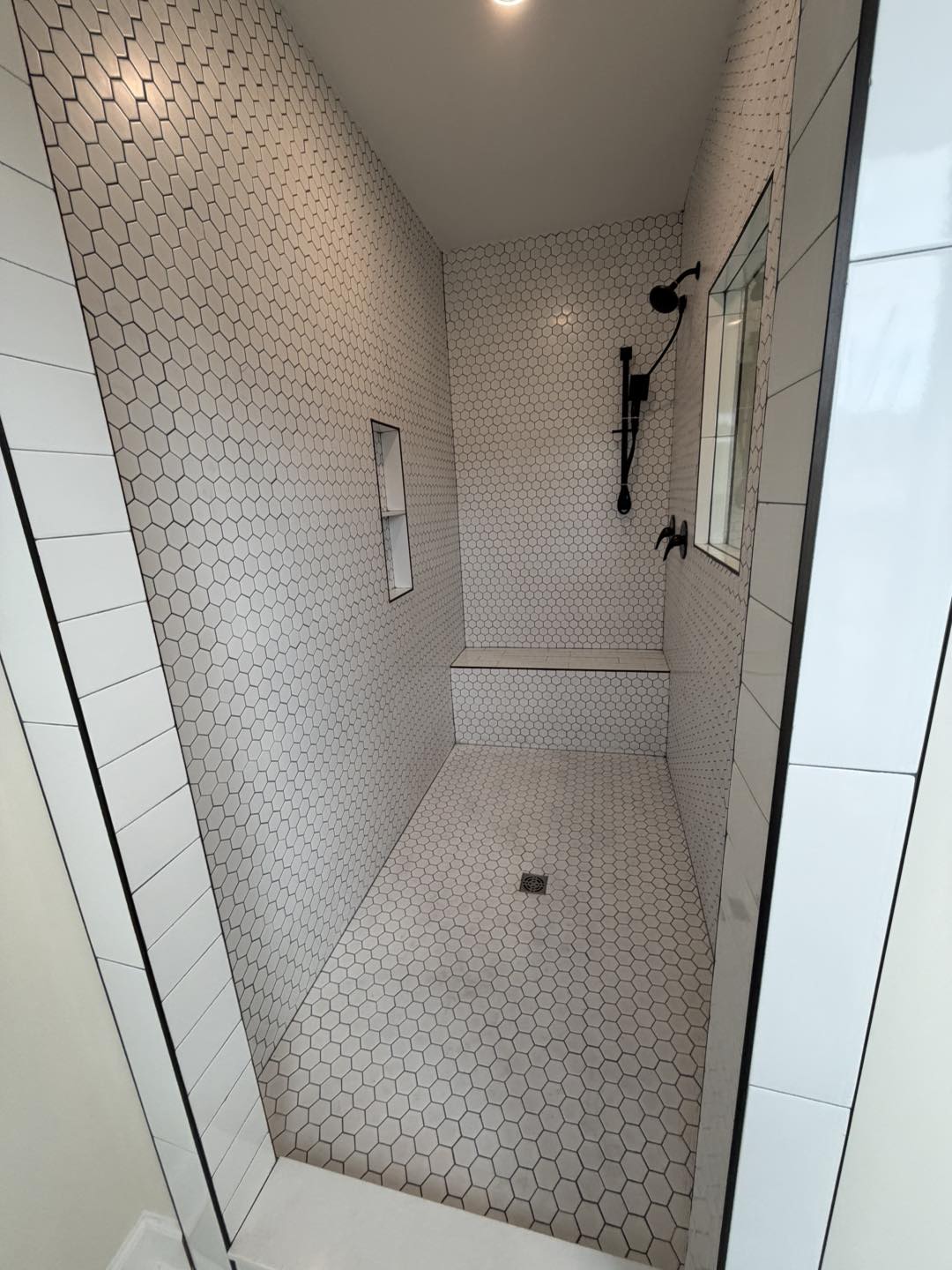 Hexagonal-tiled shower with recessed shelf, window, and dark fixtures. Clean, modern design with a minimalist, serene ambiance.