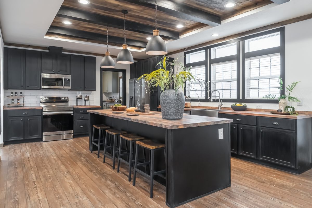 Spacious modern kitchen with dark cabinets, wooden countertops, and a large island. Pendant lights hang above the island, plants add a fresh touch.
