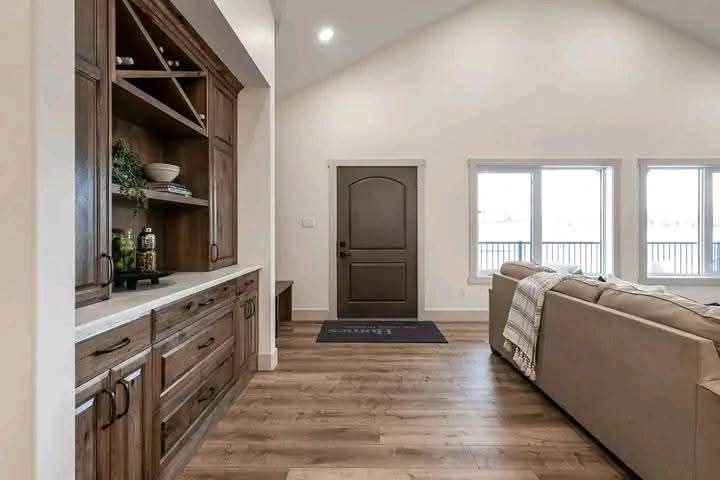 Cozy living room with wooden floors, a beige sofa draped with a blanket, built-in wooden shelving, and a dark wooden door, creating a warm ambiance.