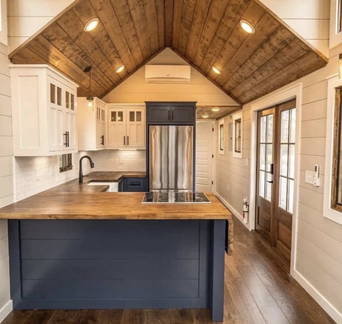 Warm, rustic kitchen with vaulted wooden ceiling, modern steel refrigerator, dark blue island, and wood countertops. Bright and inviting ambiance.