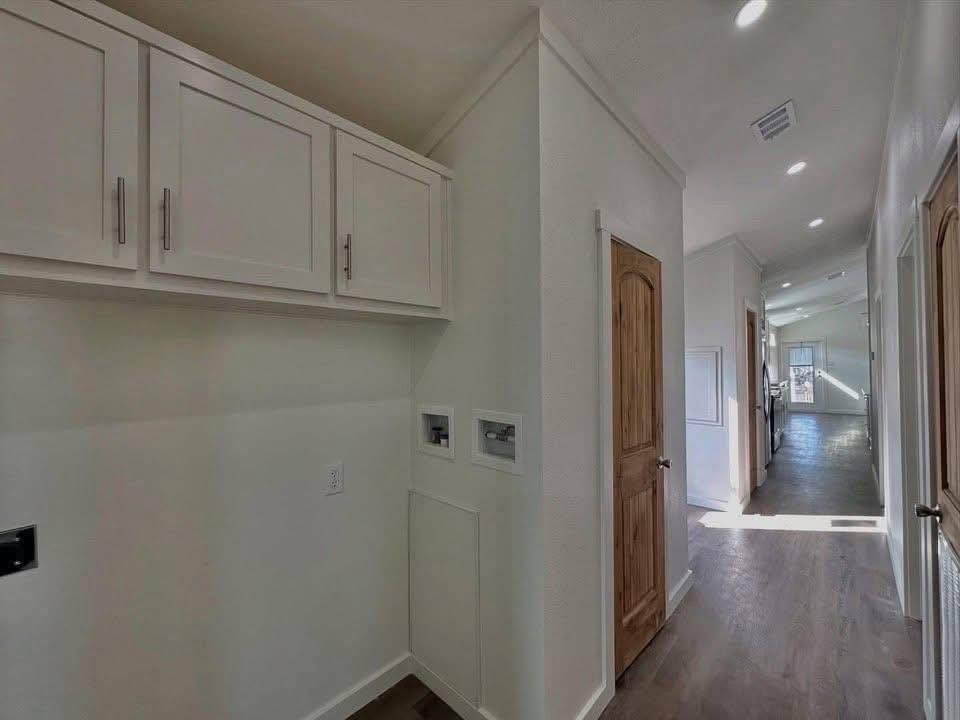 Hallway with wooden floors and bright natural light. White cabinets are on the left, and a wooden door is on the right. Minimalist and airy ambiance.