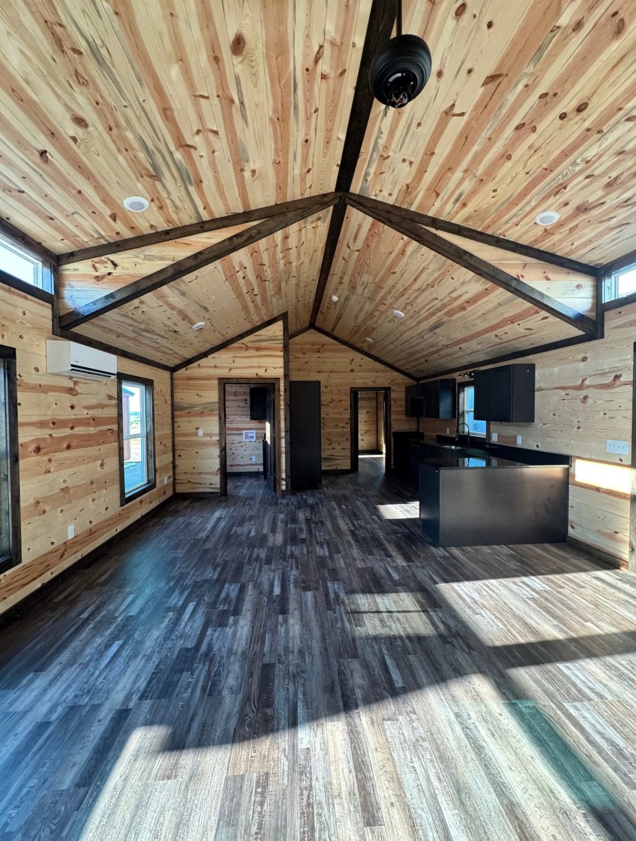 Spacious wood-paneled room with high vaulted ceilings and dark wood beams. Sunlight streams in, highlighting the dark cabinets and flooring. Cozy, rustic ambiance.