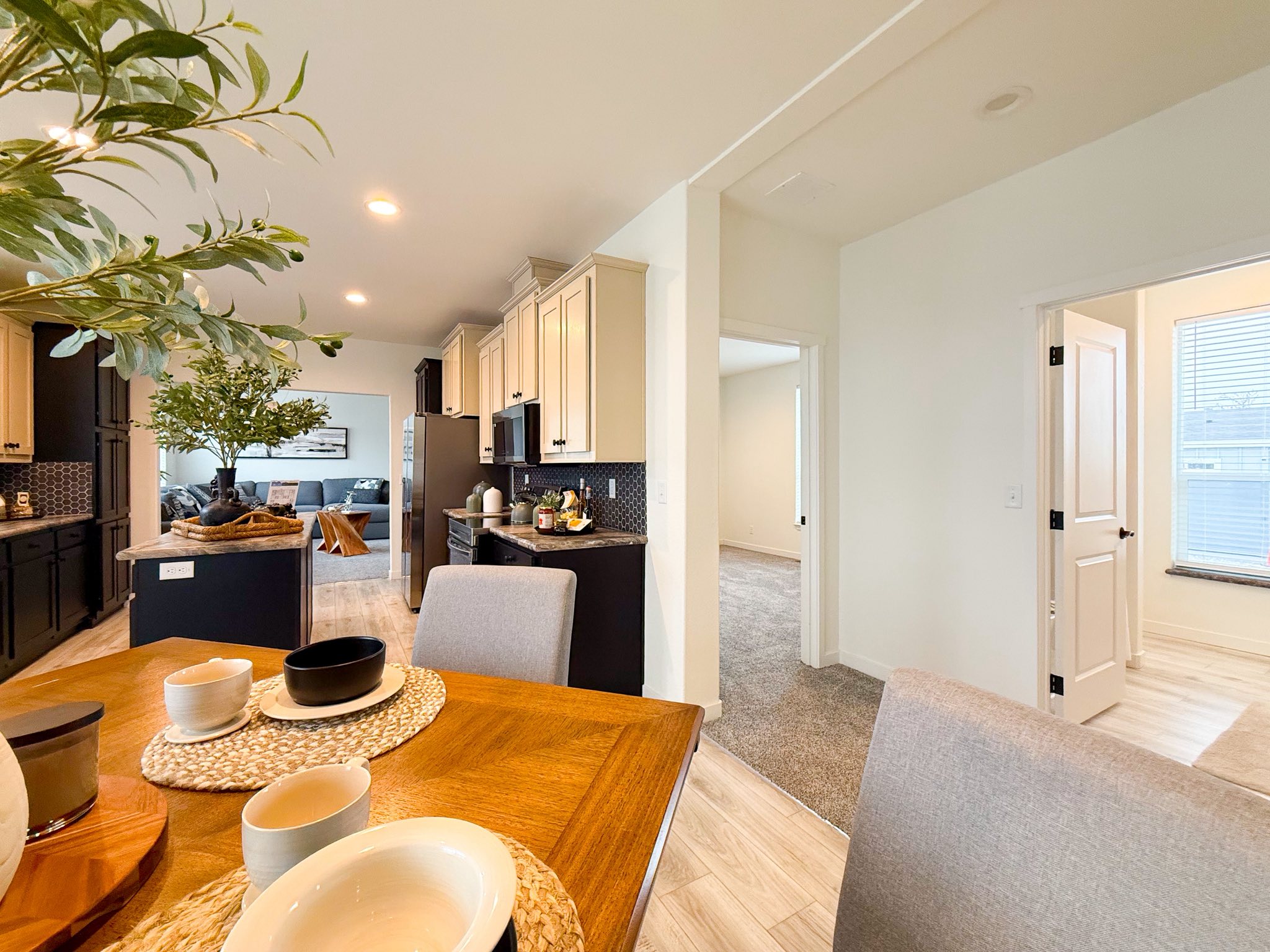 Modern open-plan kitchen and dining area, featuring a wooden table set with bowls and mugs. Neutral tones, plants, and ample natural light create a welcoming atmosphere.