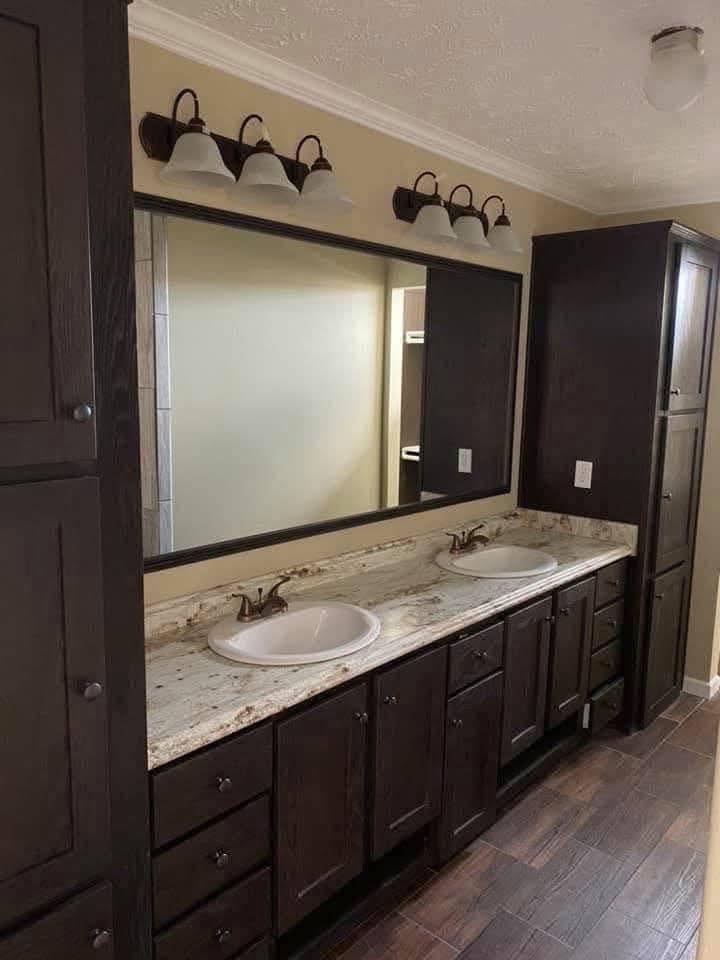 Modern bathroom with dark wood cabinets, dual sinks, and a marble countertop. A large mirror and three-light fixtures enhance the elegant design.