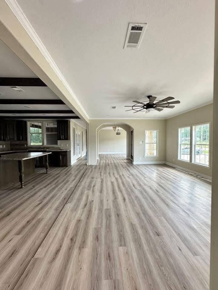 Spacious, modern kitchen and living area with light wood flooring, large windows, and ceiling fan. Dark wood kitchen cabinets create contrast.