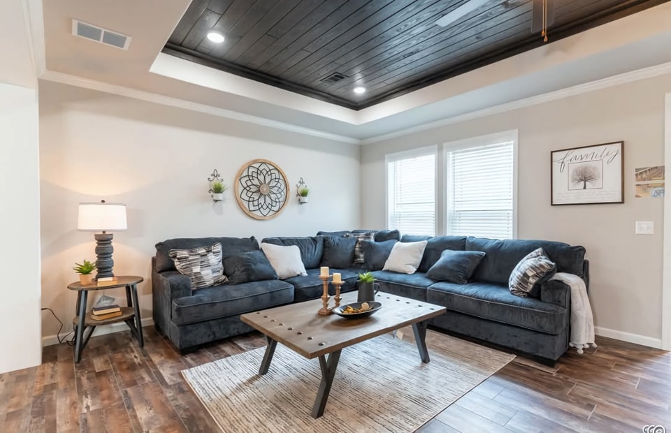 A cozy living room with a large navy sectional sofa adorned with white pillows, a wooden coffee table, soft lighting, and decorative wall accents, creating a warm and inviting atmosphere.