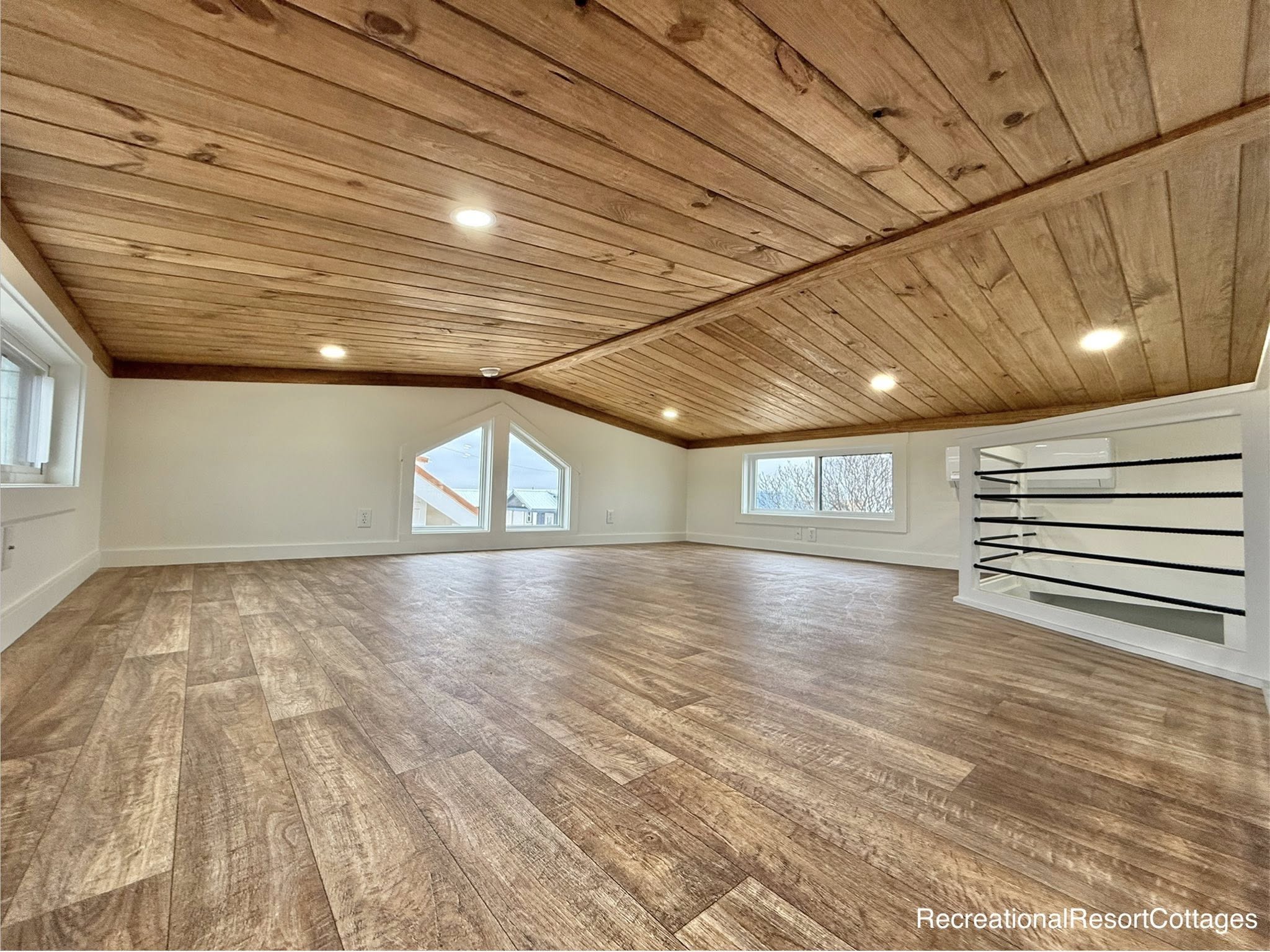 Cozy loft with sloped wooden ceiling, warm wood floors, and angled windows. Bright and inviting space evokes a sense of comfort and tranquility.