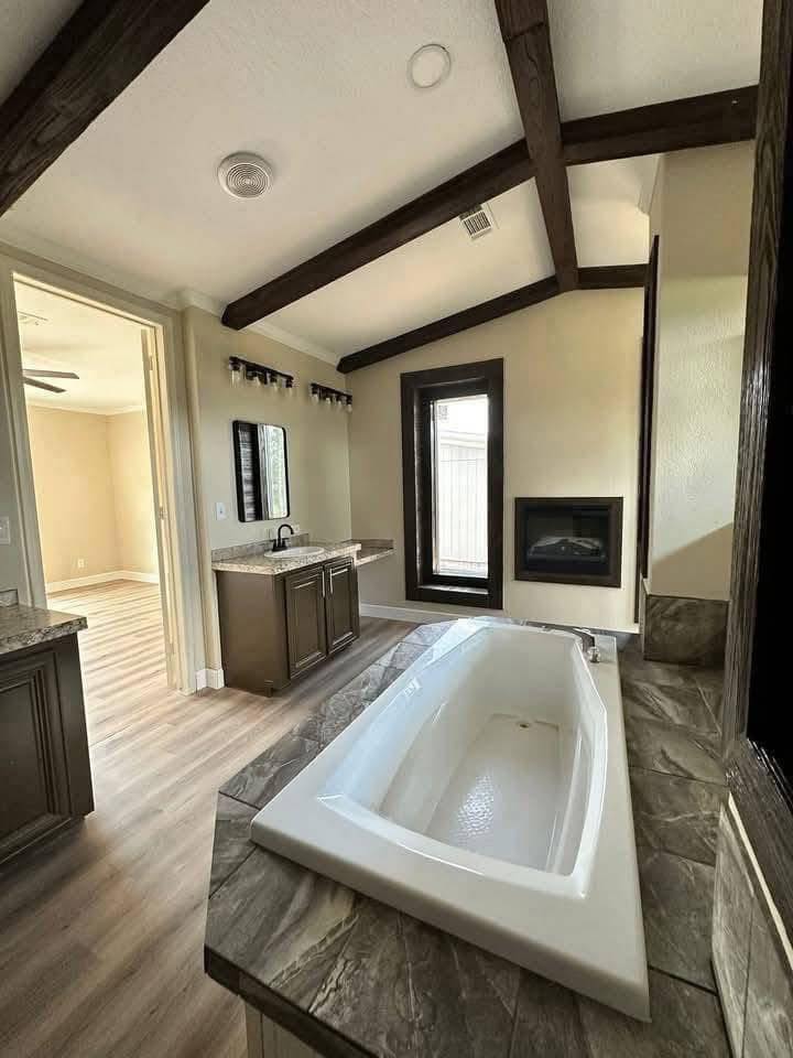 Luxurious bathroom with dark wooden beams, a large modern bathtub on a stone platform, and elegant countertop sinks; warm and inviting atmosphere.