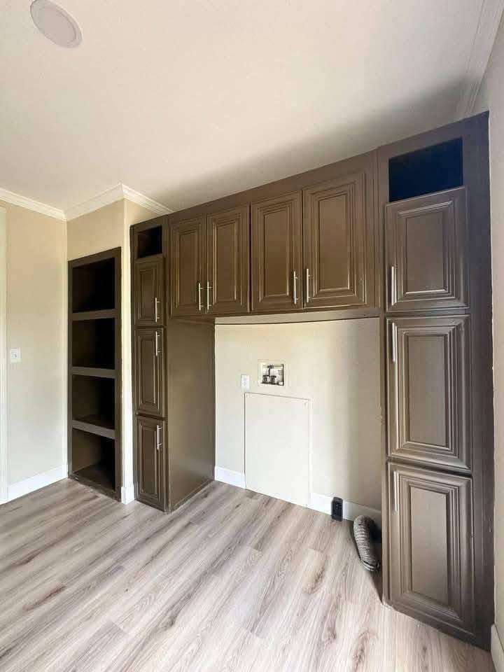 Built-in laundry nook with dark brown cabinets and open shelving on a light wood floor. The atmosphere is clean and organized, ready for installation.