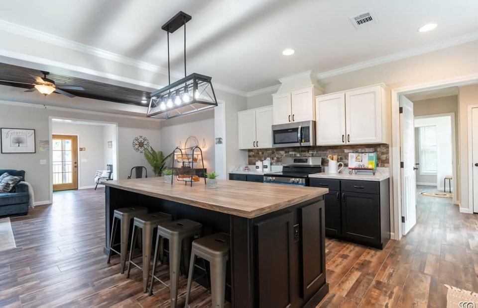 Spacious kitchen with a large island featuring dark cabinets and wood countertops. Pendant lights hang above, with stools tucked underneath. Bright and modern.