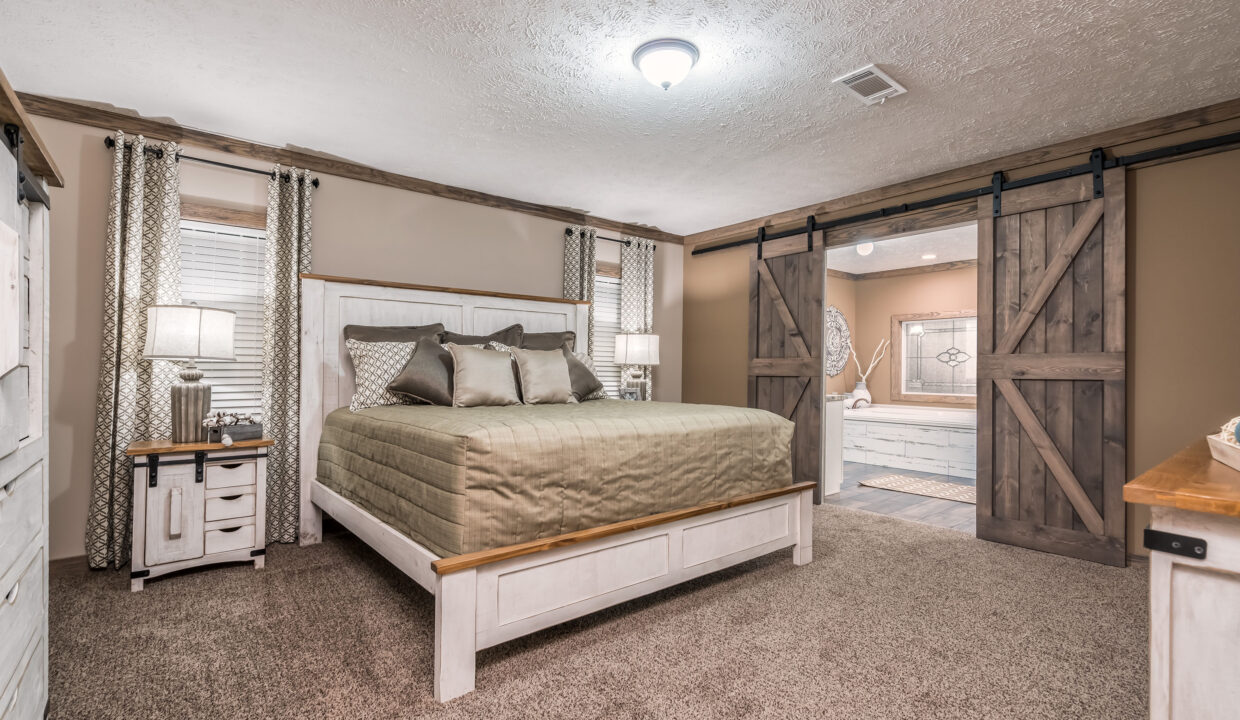 Cozy bedroom with a large bed, green bedding, and wooden headboard. Barn doors lead to a bathroom, creating a rustic and inviting ambiance.