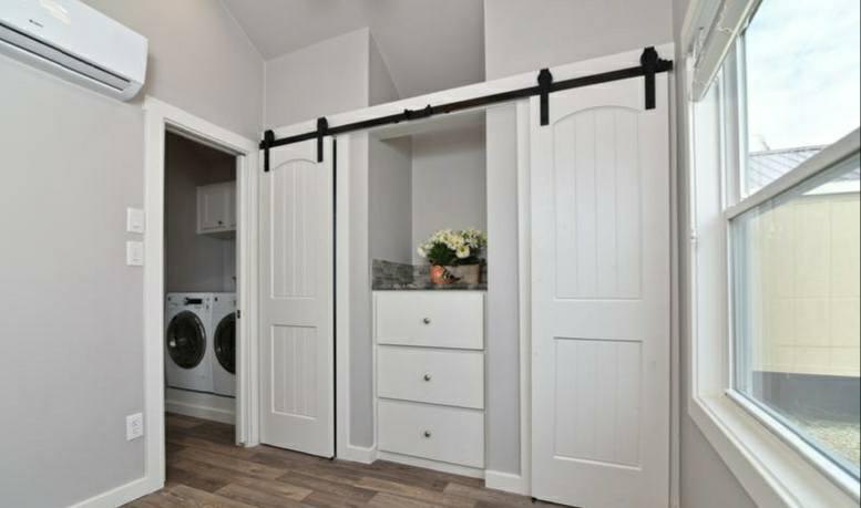 A bright laundry room with sliding barn doors, revealing a washer and dryer on the left and white drawers with flowers on top in the center.