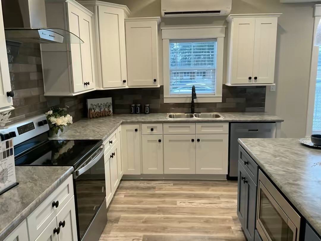 Modern kitchen with white cabinets, marble countertops, and stainless steel appliances. A window above the sink lets in natural light, creating a cozy atmosphere.