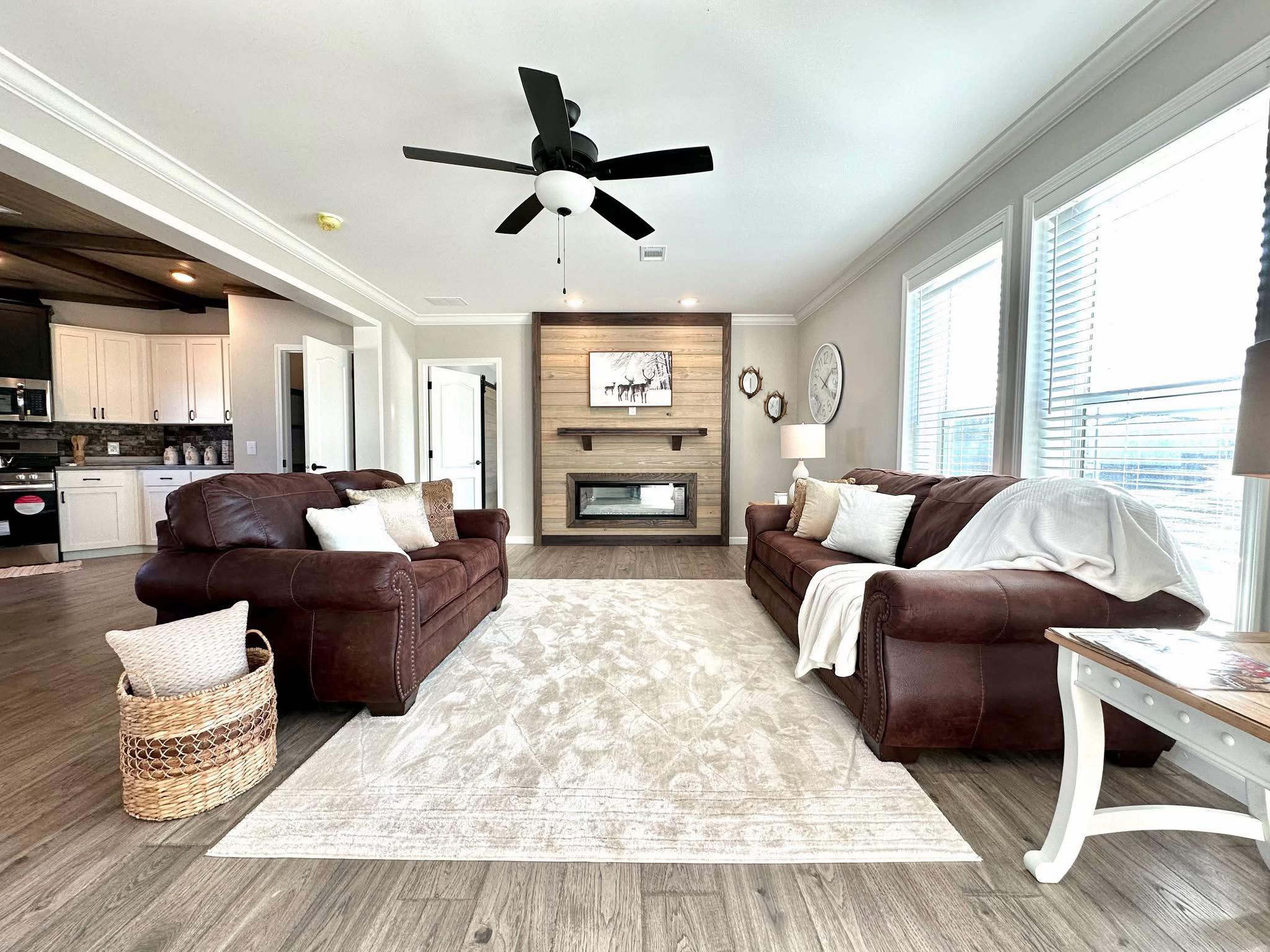 Spacious living room with brown leather sofas, a light rug, and a wooden fireplace. Large windows provide natural light, creating a cozy atmosphere.