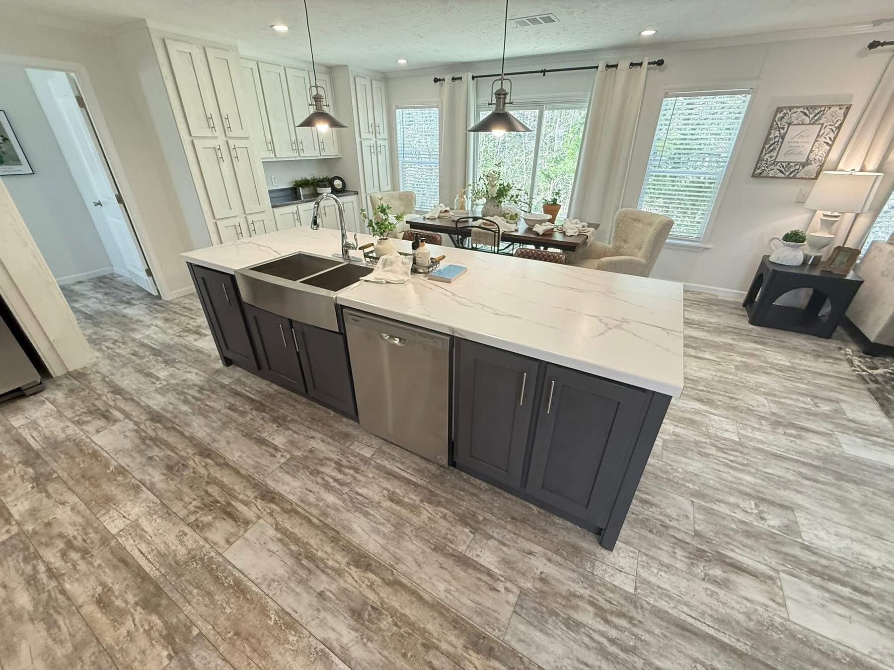 Modern kitchen and dining area with a large island featuring a marble countertop and sink. Dining table set for six. Bright, airy ambiance.