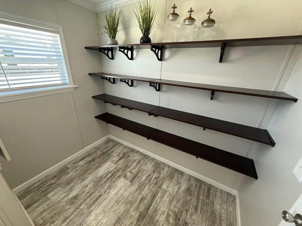 Room with five dark wooden shelves on white walls, lined with vases and greenery. Light wood flooring and a window with blinds create a minimalist, clean feel.